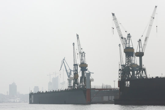Floating dock in the harbor of Hamburg. Cranes of shipyard in misty morning on the Elbe river.