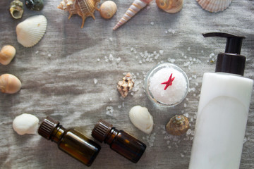 Shell, aromatherapy oil, bottle of body cream and a jar of sea salt on a grey cloth background. Spa concept.