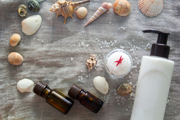 Fototapeta na wymiar Shell, aromatherapy oil, bottle of body cream and a jar of sea salt on a grey cloth background. Spa concept.