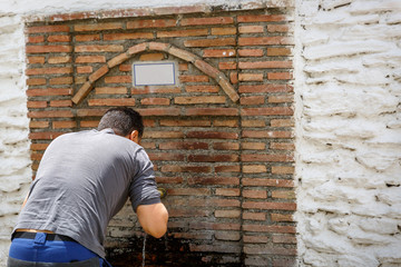 A traveler drinks water from a small fountain, in a village