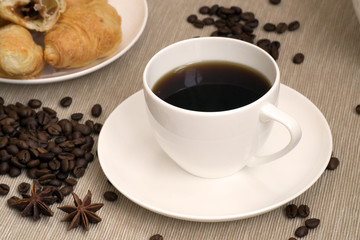 White cup of coffee and croissants with coffee beans scattered on the table
