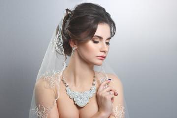 Beauty portrait of a beautiful innocent bride with veil isolated on a gray background. Wedding make up and hair