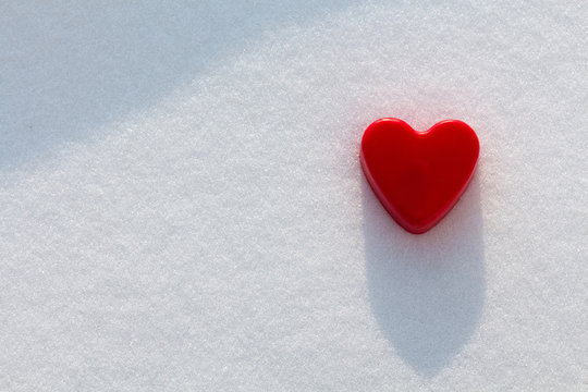 Red heart in the snow with sunshine