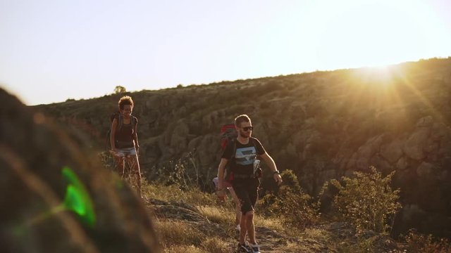 Bearded male wearing backpack and black sunglasses with two females walking outdoors with map in slowmotion