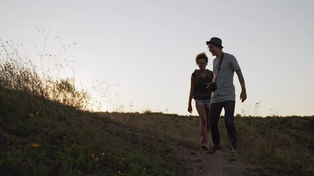Caucasian male with camera glasses and hat alking outdoors with dark-skinned female with backpack in slowmotion