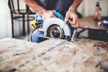 Carpenter using circular saw for cutting wooden boards. Construction details of male worker or...