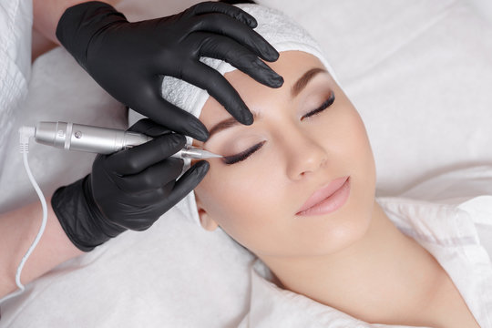 Professional cosmetologist wearing black gloves making permanent makeup