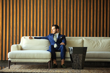 Happy young businessman sitting relaxed on sofa at hotel lobby using smartphon, waiting for someone.