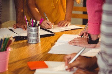 Mid section of business executives writing in book