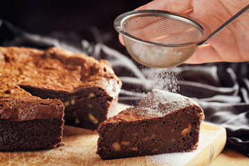 Hands holding sieve with powdered sugar and sprinkling cake