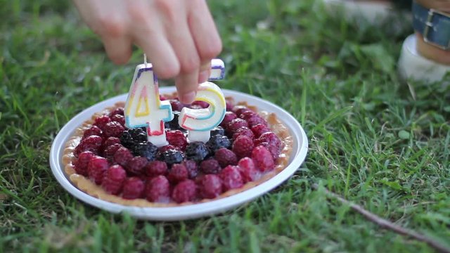 Woman hands take plate with berry cake with candles in the form of numbers 45