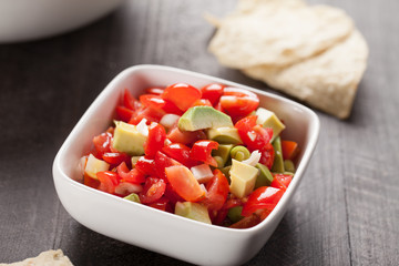 Small white bowl of homemade salsa with chips on a dark wooden background horizontal shot