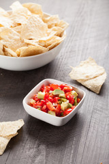 Small white bowl of homemade salsa with chips on a dark wooden background vertical shot