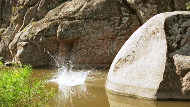 Caucasian tattoed male jumping with running start from great rock to lake than swimming away smiling. In slowmotion