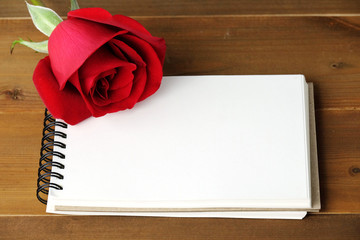 Red rose and blank note book paper on wood background