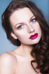 Beautiful brunette woman with creative make up violet eye shadows full red lips, blue eyes and curly hair with her hand on her face