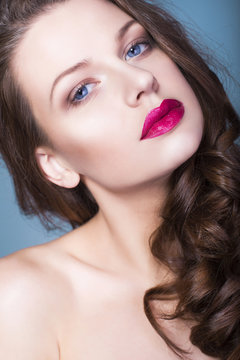 Beautiful brunette woman with creative make up violet eye shadows full red lips, blue eyes and curly hair with her hand on her face
