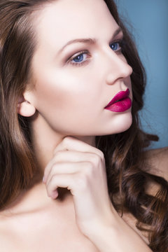 Beautiful brunette woman with creative make up violet eye shadows full red lips, blue eyes and curly hair with her hand on her face