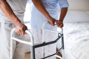 Senior woman helping senior man to walk with walker at home