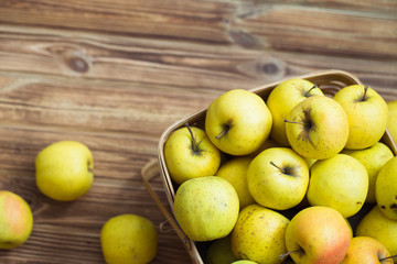 Golden apples in a basket on a wooden background