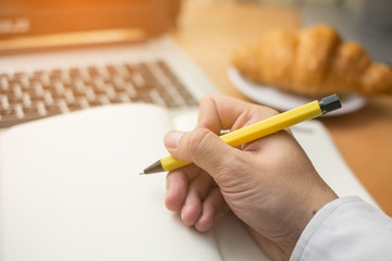 hand's man wrote message on white notebook with yellow pen and croissant on wood table, business vintage concept