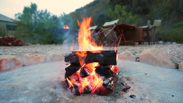 A campfire burns in a fire pit at a safari camp
