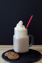 Vertical background with hot chocolate topped with whipped cream and red straw served on a trendy black slate board with two chocolate cookies