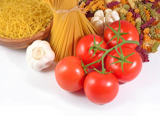 Ripe tomatoes branch, uncooked Italian pasta and garlic on a whi