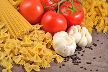 Uncooked Italian pasta, ripe tomatoes branch, garlic and black p