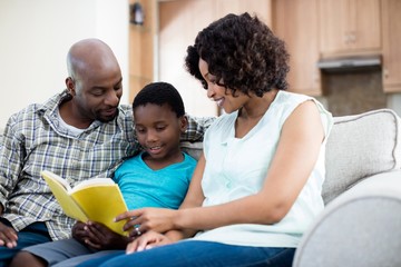 Parents reading book with their son in living room