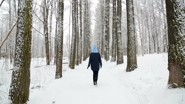 girl walking in the woods in the grove back in the blue hat and dark jacket