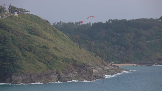 Three persons are paragliding near wind mill and one is preparing the parachute. Great landscape view with sea shore and sportsmen in 4k
