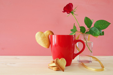 Cup of coffe with cookies next to one red rose in the vase