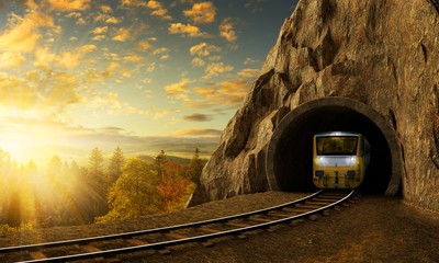 Mountain railroad with train in tunnel in rock above landscape.