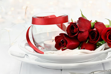 Romantic candlelight table setting with long stem red roses and candles in the background. Shallow depth of field with selective focus on roses.