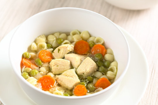 Homemade chicken soup with pea, carrot and small shell pasta in bowl, photographed with natural light (Selective Focus, Focus in the middle of the soup)