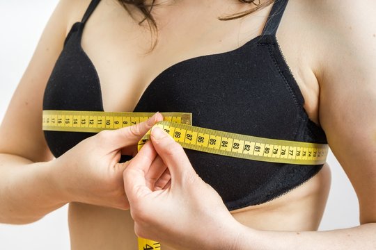 Woman is measuring her breast size with a tape.