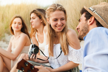 Beach at sunset in summer. Group of young friends are to relax, man plays guitar while the beautiful women smile