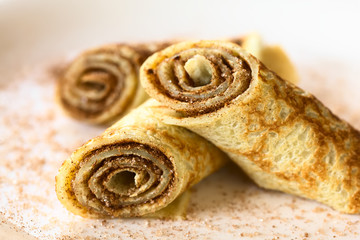 Crepe rolls filled with cinnamon and sugar, photographed with natural light (Selective Focus, Focus on the front lower edge of the right roll, and on the top edge of the left roll) © Ildi