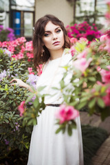 Beautiful brunette woman in flower garden with red pink azalea in a sensual dress