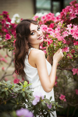 Beautiful brunette woman in flower garden with red pink azalea in a sensual dress