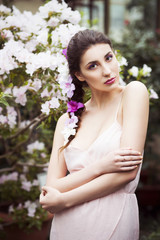 Beautiful brunette woman in flower garden with red pink azalea in a sensual dress