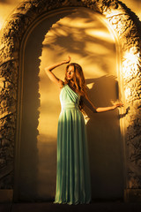 Beautiful blonde with a long curly hair in a long evening dress in static outdoors near retro...