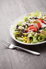 Black bean, corn, and tomato southwest salad on a dark wooden background with fork