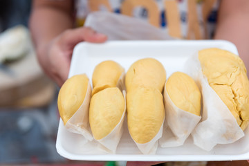 merchant's hands holding pieces of durian on white plastic tray