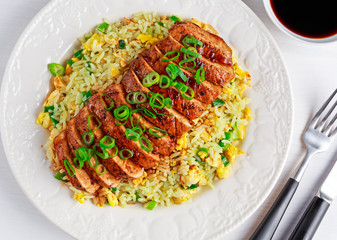 Chinese style Egg fried rice with sliced pork fillet on white wooden table.