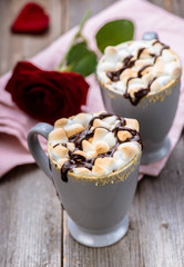S'mores drink. Two mugs of hot chocolate with marshmallows on a wooden table. Cocoa. Rose petals. Valentine.