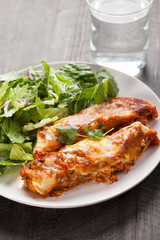 Spicy chicken enchiladas with a side of light green salad on a dark wood background vertical shot