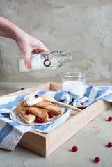 beautiful russian pancakes with sour cream, cranberry and bottle of fresh milk on concrete background