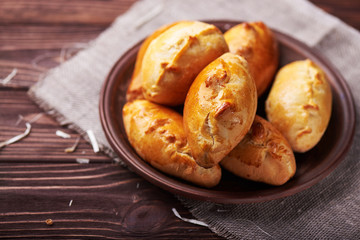 Delicious rustic pastries filled with meat and vegetables on a ceramic plate with wooden on a wooden background.